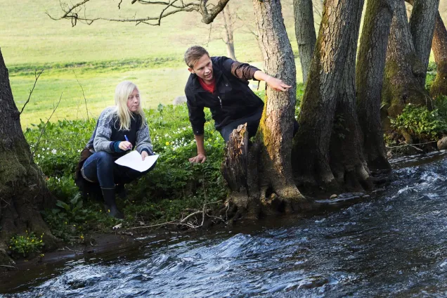 Two people looking at a stream. Photo.